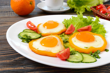 Fried egg in a circle of sweet pepper on a white plate with fresh vegetables, a cup of coffee, fresh oranges on a wooden background. Delicious healthy breakfast. Proper nutrition.