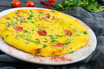 Frittata. Italian omelette with cheese, greens and tomatoes on a white plate on a wooden background.
