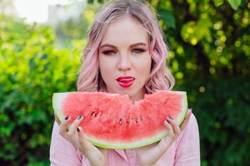 Beautiful young woman with pink hair enjoying watermelon