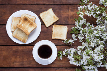 Toast, coffee and blossoming cherry branches on a wooden background.