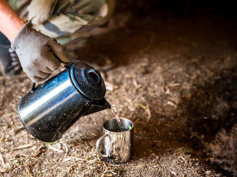 Wasser mit einer alten Blech Kaffekanne in einen Becher gie&szlig;en 