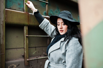 Brunette girl in gray coat with hat in railway station.