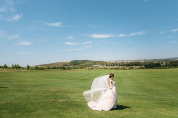 Beautiful bride in luxury fashion white wedding dress with veil on the green golf club glade, wedding day. Amazing full length body portrait of girl. Marriage concept.