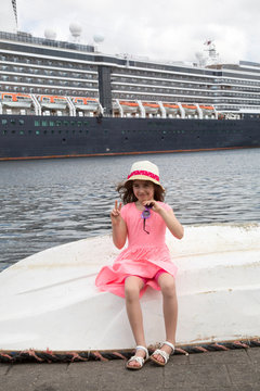 Kind sitzt auf Boot - im Hintergrund Kreuzfahrtschiff