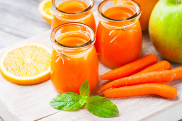 Jars with carrot juice, apple, sliced orange and mint leaf 