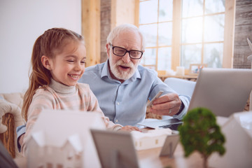 Home schooling. Positive aged man sitting near his pupil while giving her a lesson