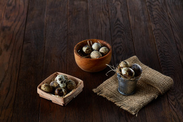 Rustic still life with quail eggs in bucket, box and bowl on a linen napkin over wooden background, selective focus