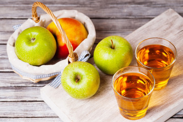 Apple juice in glasses and apples in a wicker basket on wooden table 