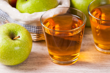 Apple juice in glasses and apples in a wicker basket on wooden table 