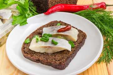 Open sandwich with pickled herring slices on brown bread closeup