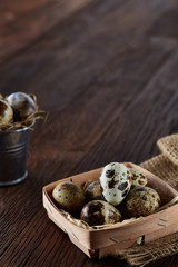 Rustic still life with quail eggs in bucket, box and bowl on a linen napkin over wooden background, selective focus