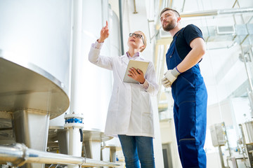 Low angle view of bearded factory worker wearing overall listening to female inspector with concentration while giving tour of production department