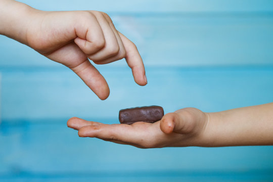 The Child Holds A Chocolate Candy In The Palm Of His Hand, Sharing It With His Friend