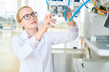 Waist-up portrait of hard-working technician wearing white coat adjusting equipment of modern dairy factory, interior of spacious production department on background