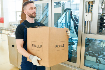 Portrait shot of confident worker wearing overall and handling gloves carrying cardboard box and...