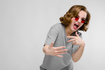 Charming young girl in a gray T-shirt on a gray background. Girl in red square-eyed glasses. The girl leaned forward