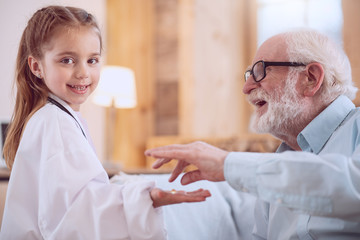 Obraz premium Dream job. Delighted positive girl smiling while giving a pill to her patient