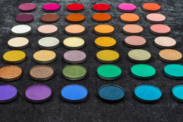 palette of professional shimmer and matt multicolored circle shaped eye shadows in straight rows on a black background. concept of professional cosmetics