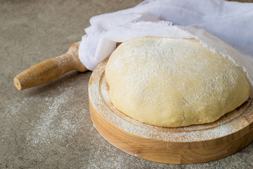 Homemade dough covered with a napkin on a round wooden board on an old table. 