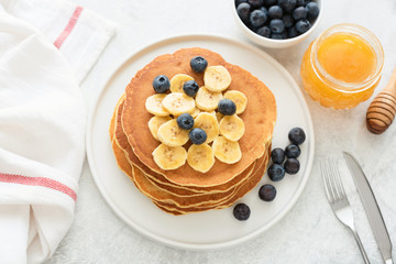 Homemade pancakes with blueberries and banana on white plate. Stack of corn pancakes. Pancakes with fruits and honey on a table
