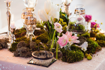 Rustic decoration (forest moss, flowers, candles, glasses and vases). Evening romantic atmosphere.