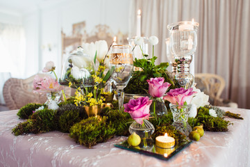 Beautiful and romantic decoration of the wedding table in rustic style (forest moss, flowers, candles, glasses and vases)