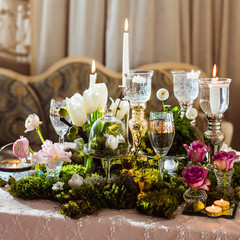 Obraz na płótnie Canvas Romantic decoration of the evening table in rustic style (forest moss, flowers, candles, glasses and vases)