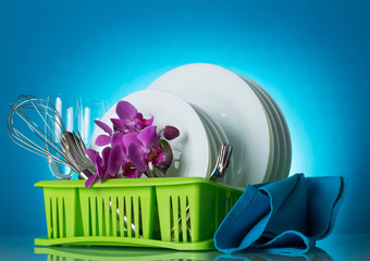 Clean plates, Cutlery and wine glasses on dryer, nearby napkin, on light blue