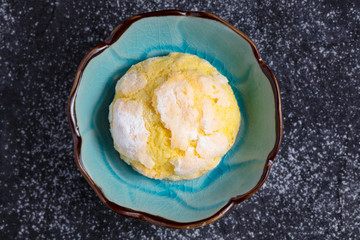 Single homemade lemon crinkle cookie with powdered sugar icing on small blue plate and dark background. Top view