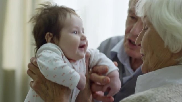 PAN of happy grandparents playing with giggling baby girl