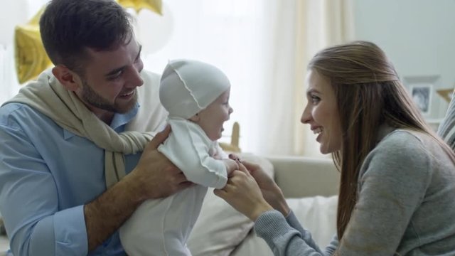 Medium shot of happy young mother playing with cute baby boy held by cheerful father