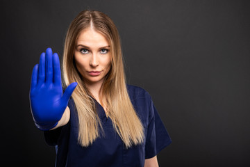 Female dentist wearing scrubs showing showing stop gesture.