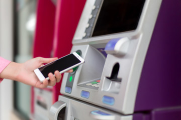 Woman holding a Smartphone financial transactions online on the background, ATM cabinet. Online NFC Banking Concept