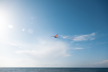 Fototapeta na wymiar Bright colorful kite in the blue sky with clouds over sea, freedom and travel concept