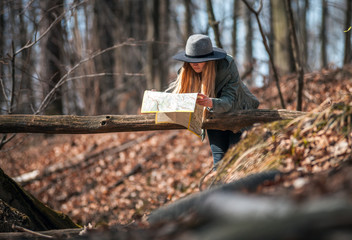 Traveler woman in hat with map in autumn forest, trekking tourism concept