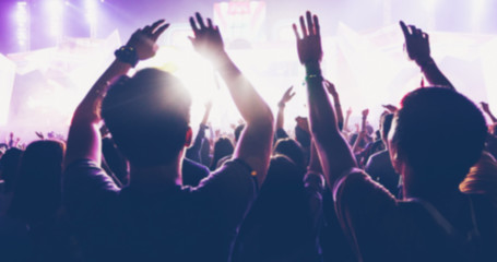 blurry of silhouettes of concert crowd at Rear view of festival crowd raising their hands on bright stage lights