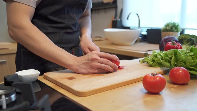 Asian man hands cutting tomato on chopping board. Close up shot of fresh vegetables on kitchen counter. Male is preparing food in kitchen at home.