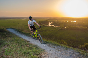 Fototapeta premium A cyclist in a white T-shirt rides a bike along the mountain path. The concept of extreme sports. Mountain bike.