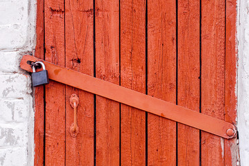 Old red wooden door locked with metal padlock.