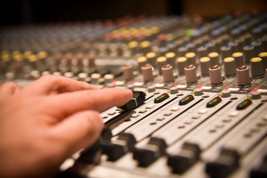 Close-up Hands Of Sound Engineer Adjusting Audio Mixer Controller For Live Music And Studio Equipment. This Is A Quality Audio System For Professionals. Vintage Tone & Effect Light In Control Room.