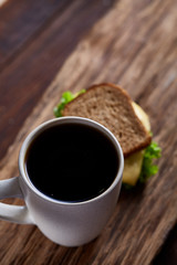 Breakfast table with sandwich and black coffee on rustic wooden background, close-up, selective focus