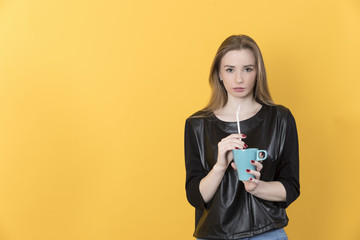 Beautiful european young girl in black jacket and jeans sits on a chair and drinks from a cup