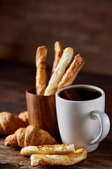 Coffee cup, breadsticks and croissants on an old wooden background, close-up, selective focus.