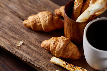 Coffee cup, breadsticks and croissants on an old wooden background, close-up, selective focus.