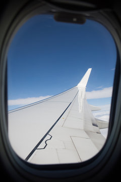 View of the plane's wing and landscape with blue sky and clouds from the window of an airplane