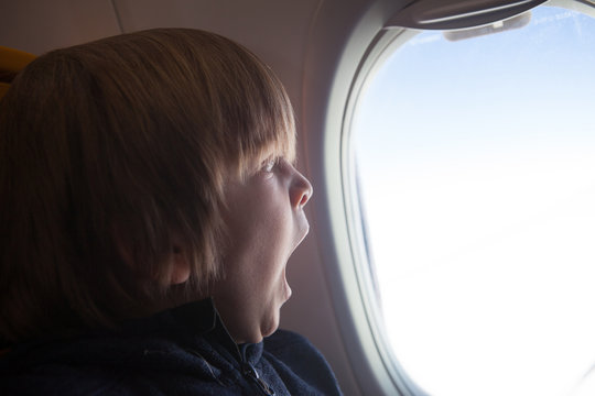 Child yawning while looking through the window of an airplane