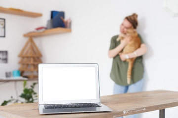 Veterinary concept. Laptop with white screen on desk on background of blurred young woman holding beautiful red cat. Place for advertising