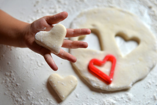 A child's hand holds a cookie in the form of a heart. Preparation of cookies. Cookies for mom