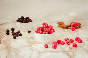 Raw raspberries and wild black, blackberries in white cups. Light marble background. Summer fruit, berries. Detox diets and healthy food concept.