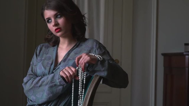 A girl with a pearl necklace sits in a chair